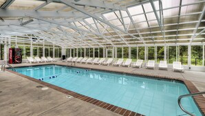 A covered swimming pool with white lounge chairs and a Coca-Cola cooler.