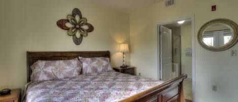 A bedroom with a wooden bed, a nightstand, a wall clock, a ceiling fan, and a mirror.
