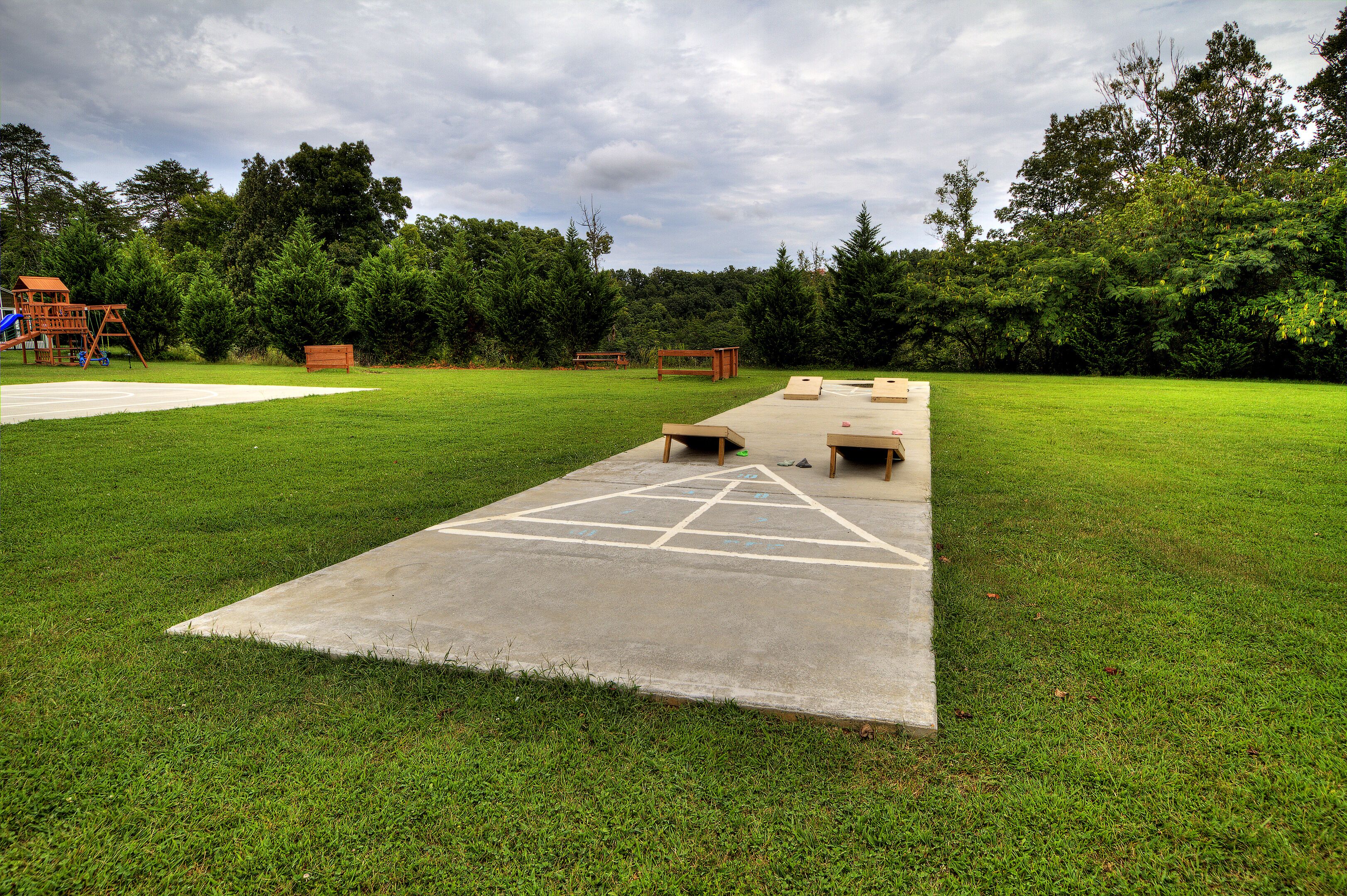 A concrete pavement with a hopscotch game, a wooden bench, and a playground structure in a grassy park area.