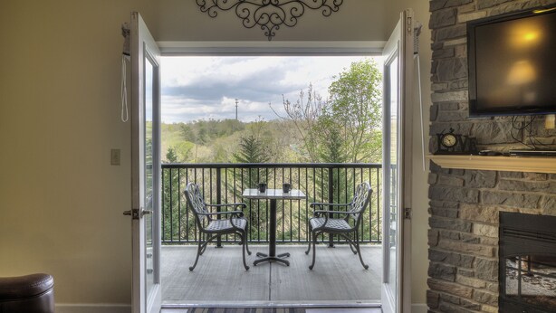 An open door leading to a balcony with a table and chairs, a stone fireplace, and a television.
