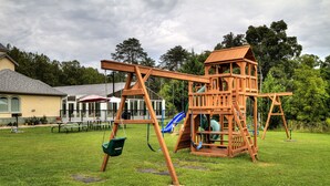 A wooden play structure with a slide and swings in a grassy yard.