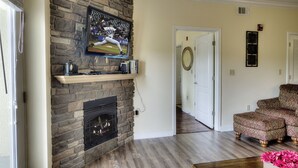 A living room with a stone fireplace, a mounted television, and a patterned armchair.