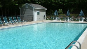A swimming pool with clear blue water, surrounded by lounge chairs and umbrellas, and a small building in the background. - Peaceful, Family Friendly, Heated Outdoor Pool, Awesome Views, Near Story Land (Bartlett)