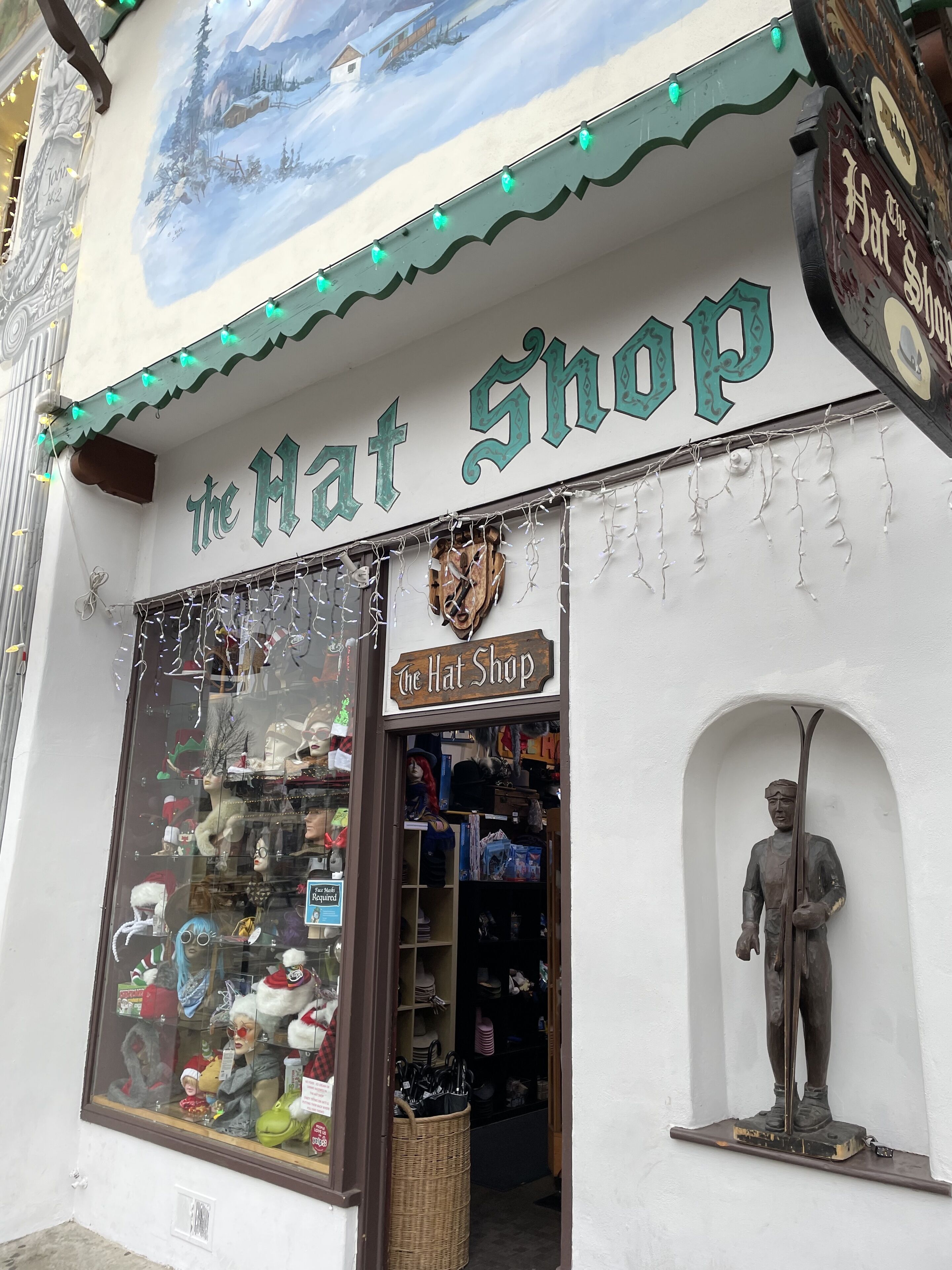 A storefront with a sign reading "The Hat Shop" and a statue of a man holding a hat.