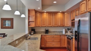 A modern kitchen with granite countertops, wooden cabinets, stainless steel appliances, and pendant lighting.