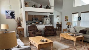 A spacious living room with a high ceiling, wooden flooring, and a kitchen in the background. - Gorgeous, near parks, 2 master suites, private pool&spa, covered patio, wifi (Davenport)