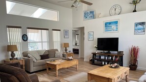 A living room with a sofa, two coffee tables, a TV, and a bookshelf. - Gorgeous, near parks, 2 master suites, private pool&spa, covered patio, wifi (Davenport)