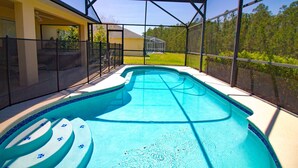 En swimmingpool med et solsejl, omgivet af et hegn, og et hus i baggrunden.