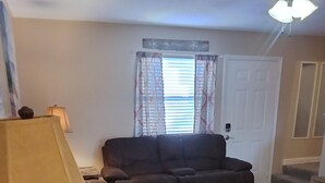 Ein Wohnzimmer mit einer braunen Couch, zwei Couchtischen, einer Lampe und einem Fenster mit Vorhängen.
