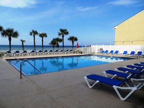A pool area with blue lounge chairs, palm trees, and a view of the ocean. - Ahh...Relax At Gulf Highlands (Panama City Beach)