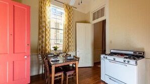 A compact kitchen with a white stove, wooden dining table, and chairs. A red door and yellow patterned curtains are visible.