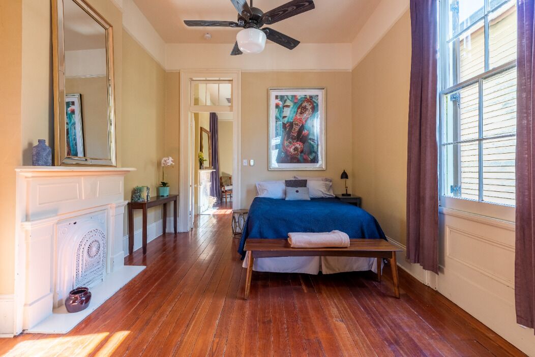 Une chambre à coucher avec un lit, un ventilateur de plafond, une cheminée, une fenêtre avec des rideaux et un tableau au mur.
