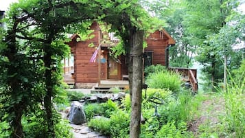 Escape to a serene cabin nestled in a lush garden, complete with a charming front porch and a tranquil atmosphere.
