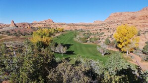 Un campo de golf con vista despejada al green, rodeado de vegetación desértica y colinas rocosas.