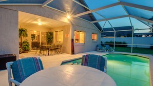 An outdoor patio area with a pool, covered seating, and a dining table.