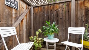 A wooden fence with a 'Beware of Dog' sign, two white metal chairs, a small round table, and a potted plant. - Bay Area Charming 1938 Art Deco Duplex (Alameda)