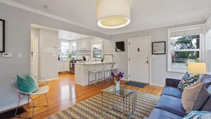 A modern living room with a sofa, a coffee table, and a dining area with a kitchen in the background. - Bay Area Charming 1938 Art Deco Duplex (Alameda)