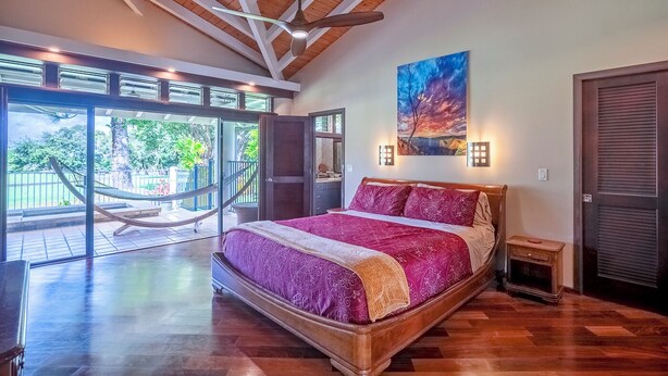 Un dormitorio amplio con una cama grande, vigas de madera en el techo y vistas al exterior, además de un cuadro en la pared.