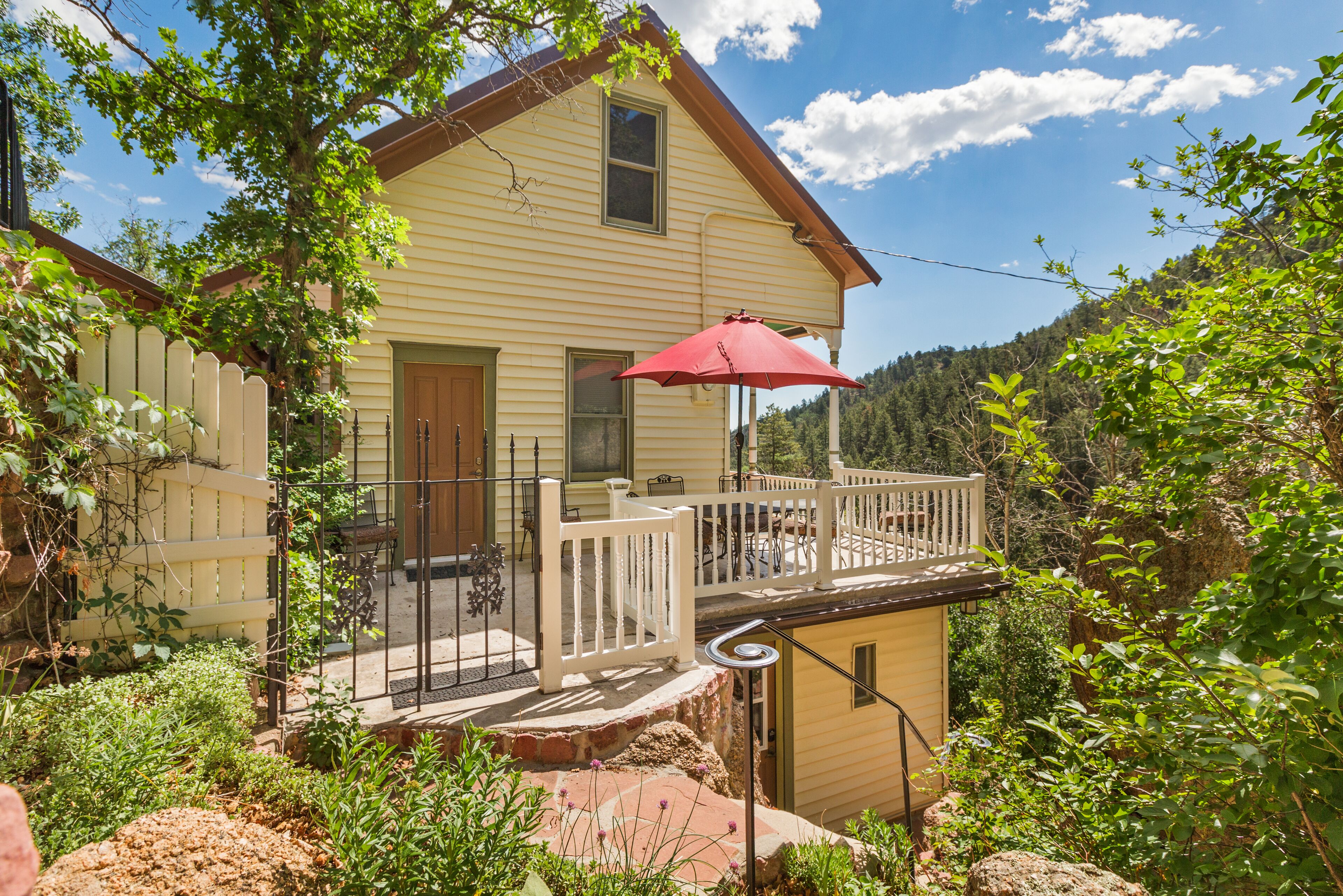 Une maison à deux étages avec un balcon, un parasol rouge et une clôture blanche en piquets.