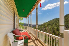A covered porch with white railings, green chairs, and a red cushion. - Borders Cog Railway, Incline, & Barr Trail ~ Closest STR to Pikes Peak Summit! (Manitou Springs)
