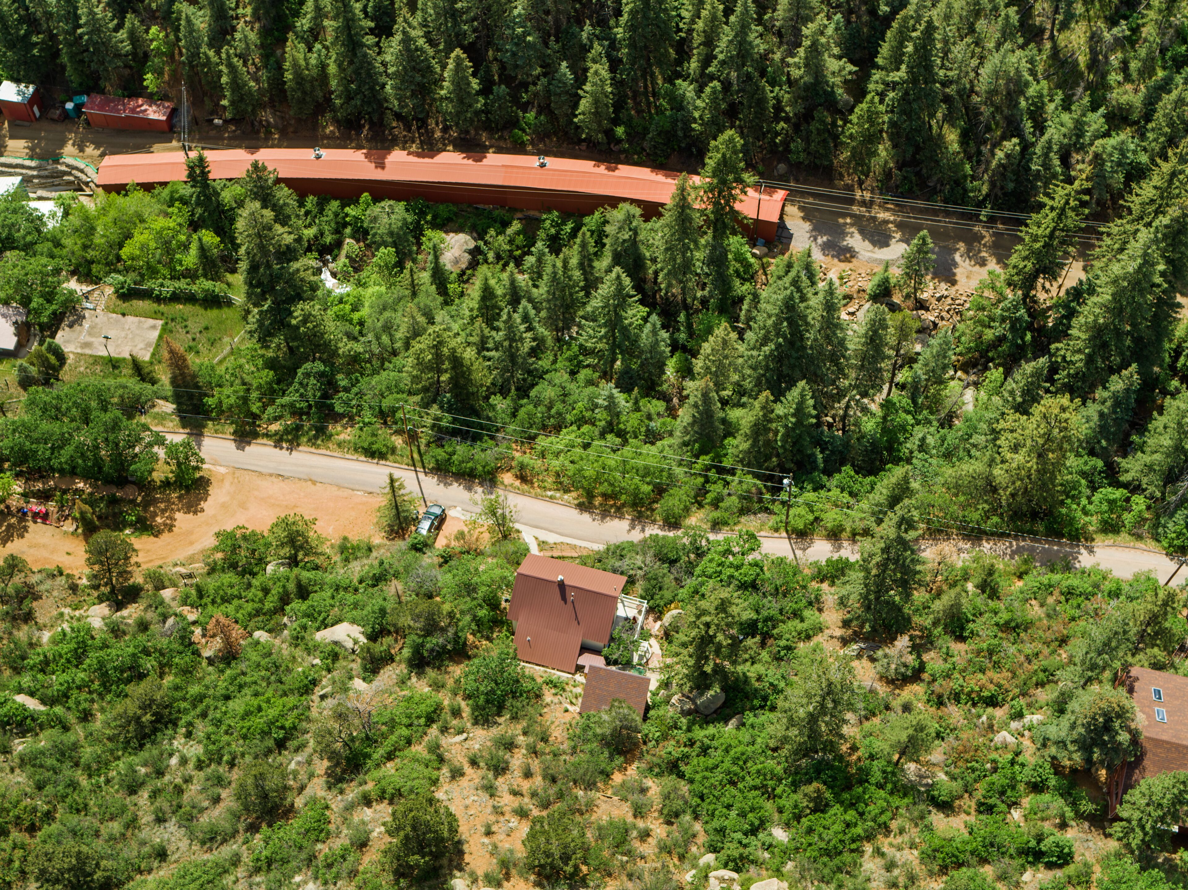 An aerial view of a residential area with a long red-roofed building, surrounded by dense green trees and a dirt road.
