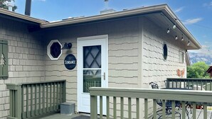 Ein Haus mit einer Terrasse, einer Tür mit der Aufschrift „SUNDAY“ und einem Schild mit einem Sechseck und einer Glocke.