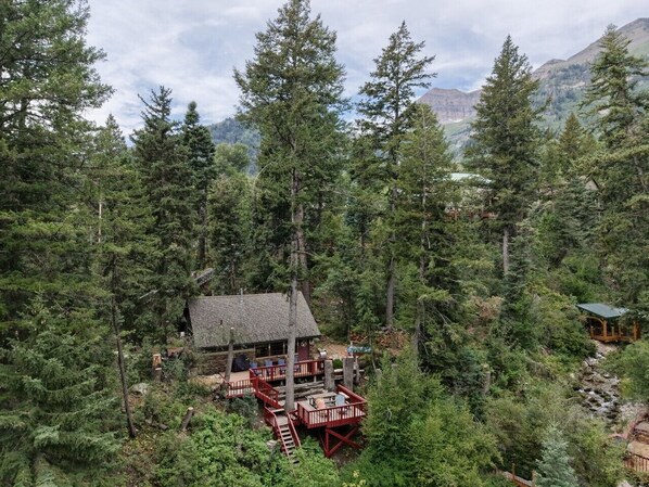 A cabin surrounded by dense forest with a deck and a small porch. - Private mountain escape • Above the creek • Hot tub • Quiet setting • Tucked into Sundance Canyon (Sundance)