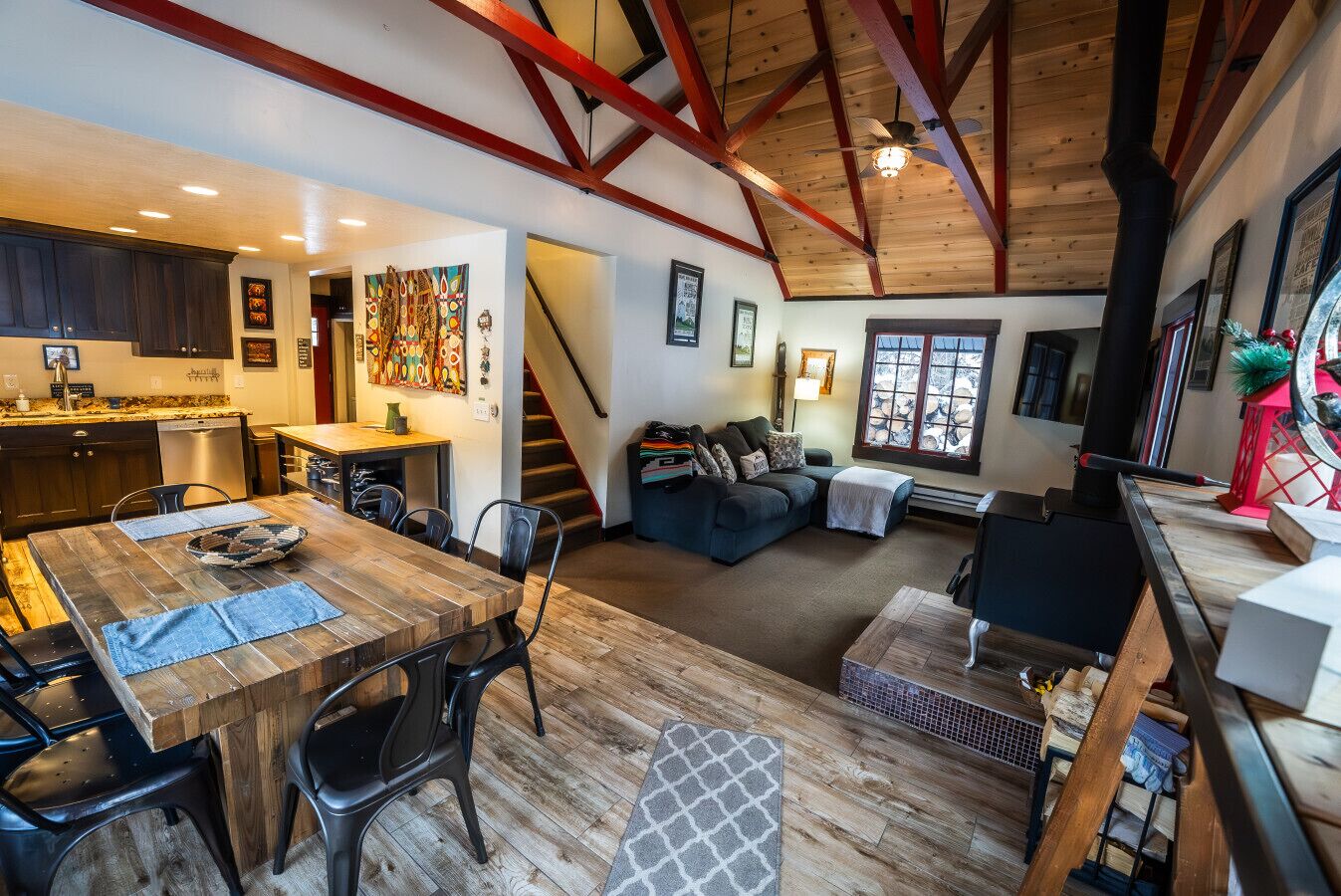 Amplia sala de estar con una mesa de comedor de madera, sillas negras, un sofá y una escalera que sube a otro nivel.