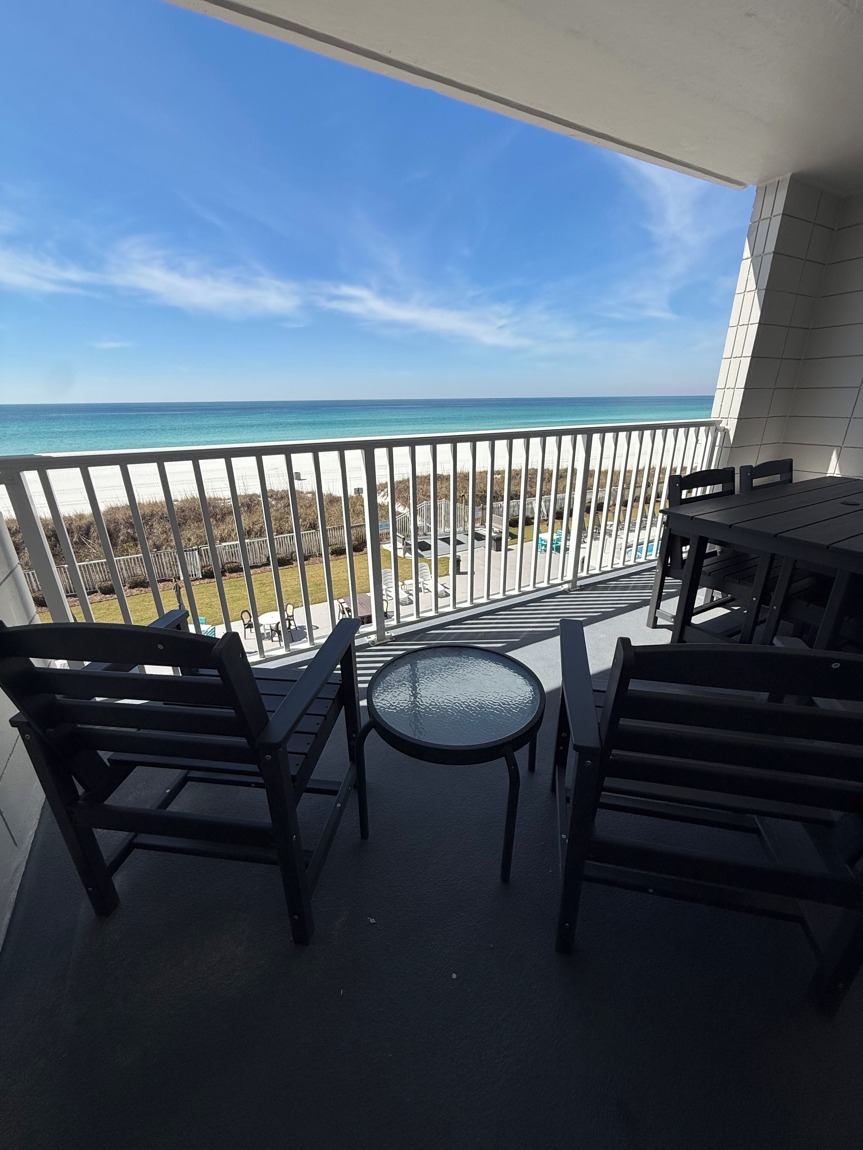 A balcony with a view of the beach and ocean, featuring a table and chairs.