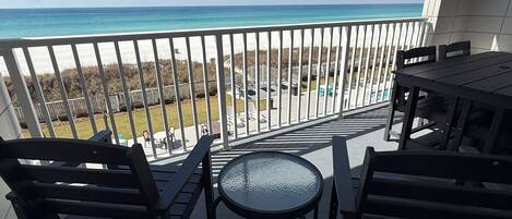 A balcony with a view of the beach and ocean, featuring a table and chairs.