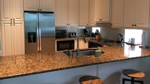A modern kitchen with white cabinets, stainless steel appliances, granite countertops, and a bar stool area.