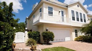 A two-story house with a front garage, a balcony on the second floor, and a well-maintained front yard with shrubs and a small tree.