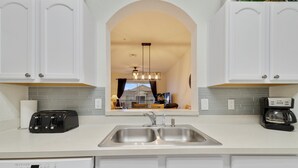 A modern kitchen with white cabinetry, a double sink, a toaster, and a coffee maker. - Tinkerbell's Hideaway 2.5 miles from Disney/pool/NO resort fees/FREE parking (Kissimmee)