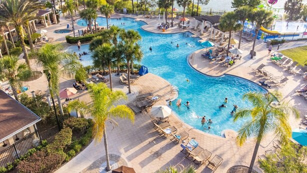 A large outdoor swimming pool with multiple lanes, surrounded by palm trees and lounge chairs. - Tinkerbell's Hideaway 2.5 miles from Disney/pool/NO resort fees/FREE parking (Kissimmee)