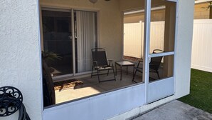 Un patio con puerta corredera de vidrio, ventilador de techo y una pequeña mesa con sillas.