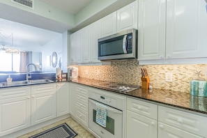 A modern kitchen with white cabinets, a stainless steel microwave, and a tiled backsplash. - Beautiful beach front condo!!! (Navarre)