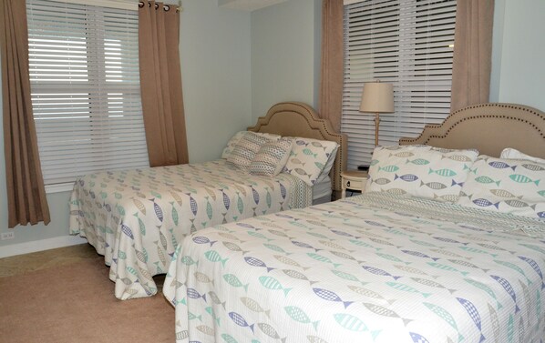 Un dormitorio con dos camas, cada una con una colcha estampada, una mesita de noche con lámpara y cortinas en las ventanas.