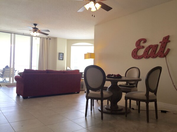 A living room with a red sofa, a dining table with chairs, and a ceiling fan.