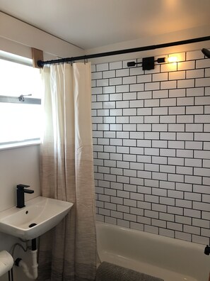 Ein Badezimmer mit einem weißen Waschbecken, einem schwarzen Wasserhahn und einer Dusche mit einer Wand aus weißen und schwarzen Fliesen.