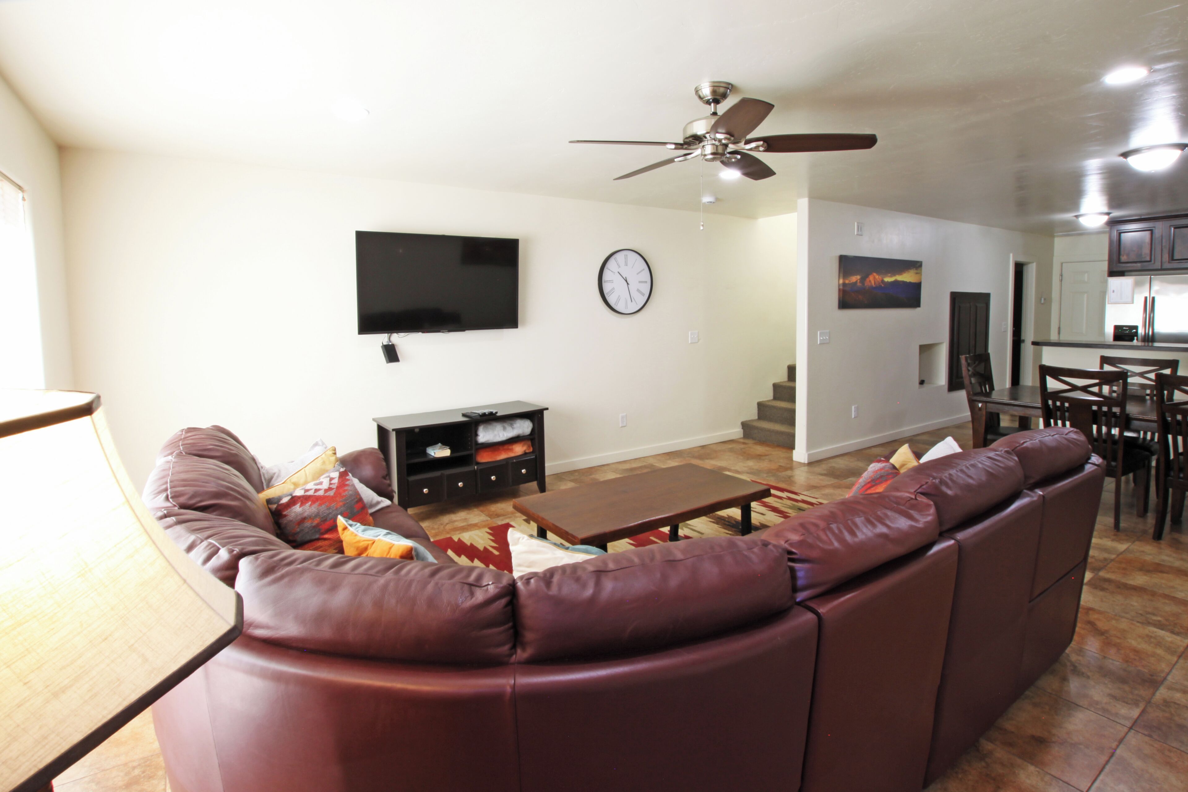 A living room with a sofa, TV, clock, and a ceiling fan.