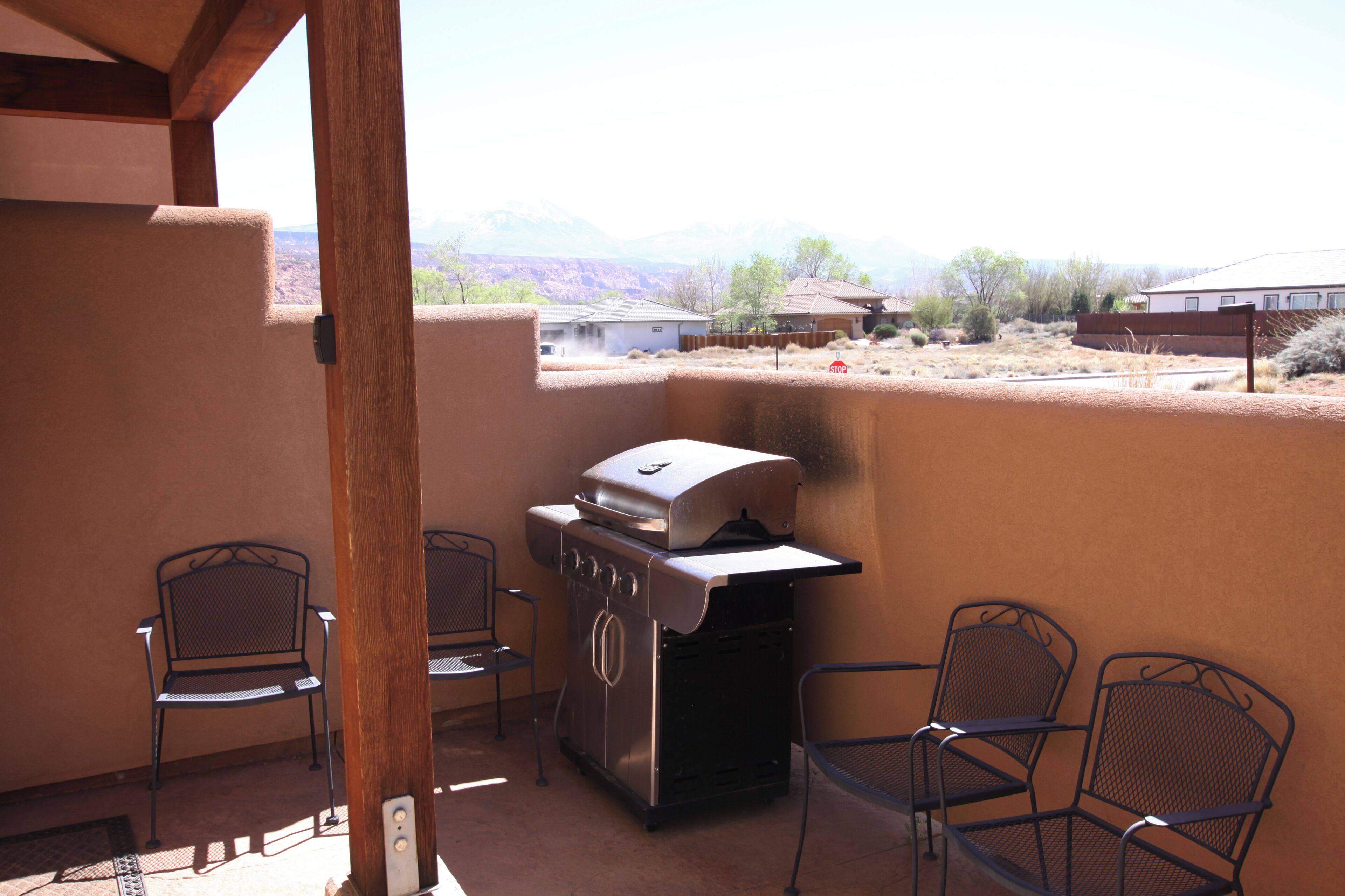 A patio with a barbecue grill, metal chairs, and a view of a residential area.