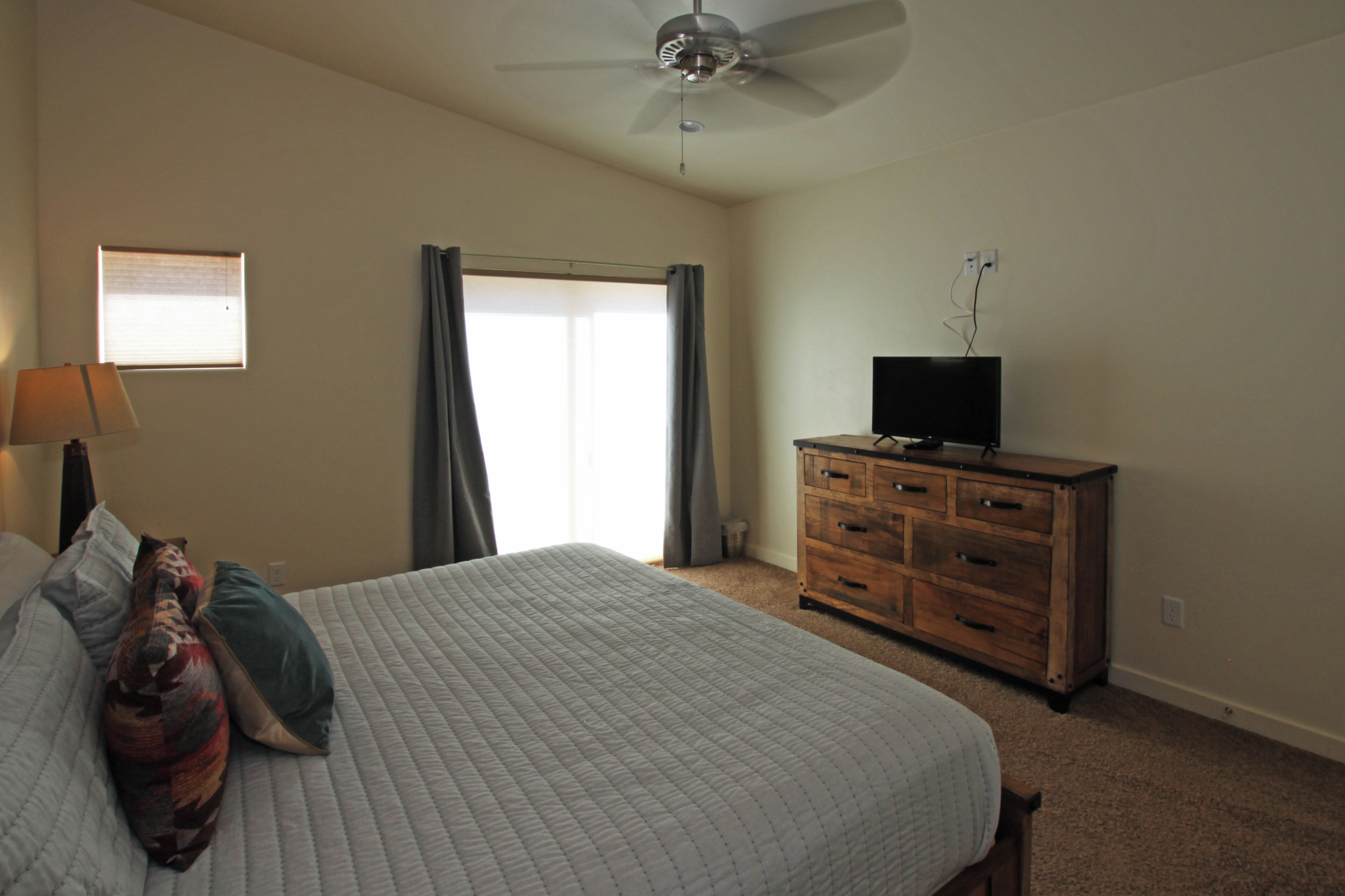 A bedroom with a bed, a dresser, a ceiling fan, a window, and a television.