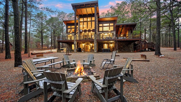 A lodge with a stone exterior, multiple decks, and a fire pit surrounded by Adirondack chairs. - 4 Bedroom 3.5 Bath-Pickleball/Basketball Court, Game Room, Hot Tub & Playground (Broken Bow)