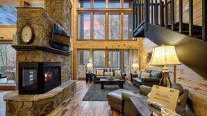 A cozy cabin interior with a stone fireplace, leather sofas, and a wooden staircase. - 4 Bedroom 3.5 Bath-Pickleball/Basketball Court, Game Room, Hot Tub & Playground (Broken Bow)