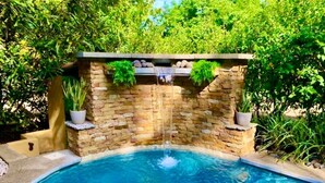 A swimming pool with a stone waterfall feature, surrounded by lush greenery.