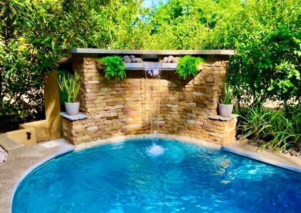 Una piscina con una cascada de piedra, rodeada de abundante vegetación.