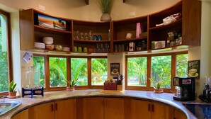 A kitchen with wooden cabinets, a granite countertop, and a view of lush greenery through large windows.