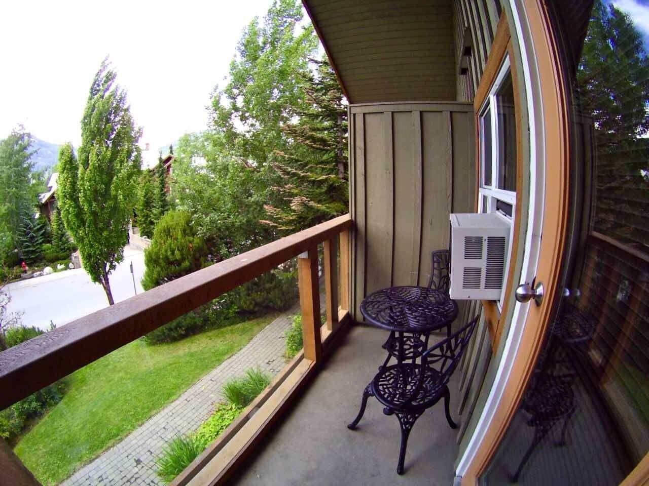 Un balcone con ringhiera in legno, un tavolino con sedie e una finestra con condizionatore.