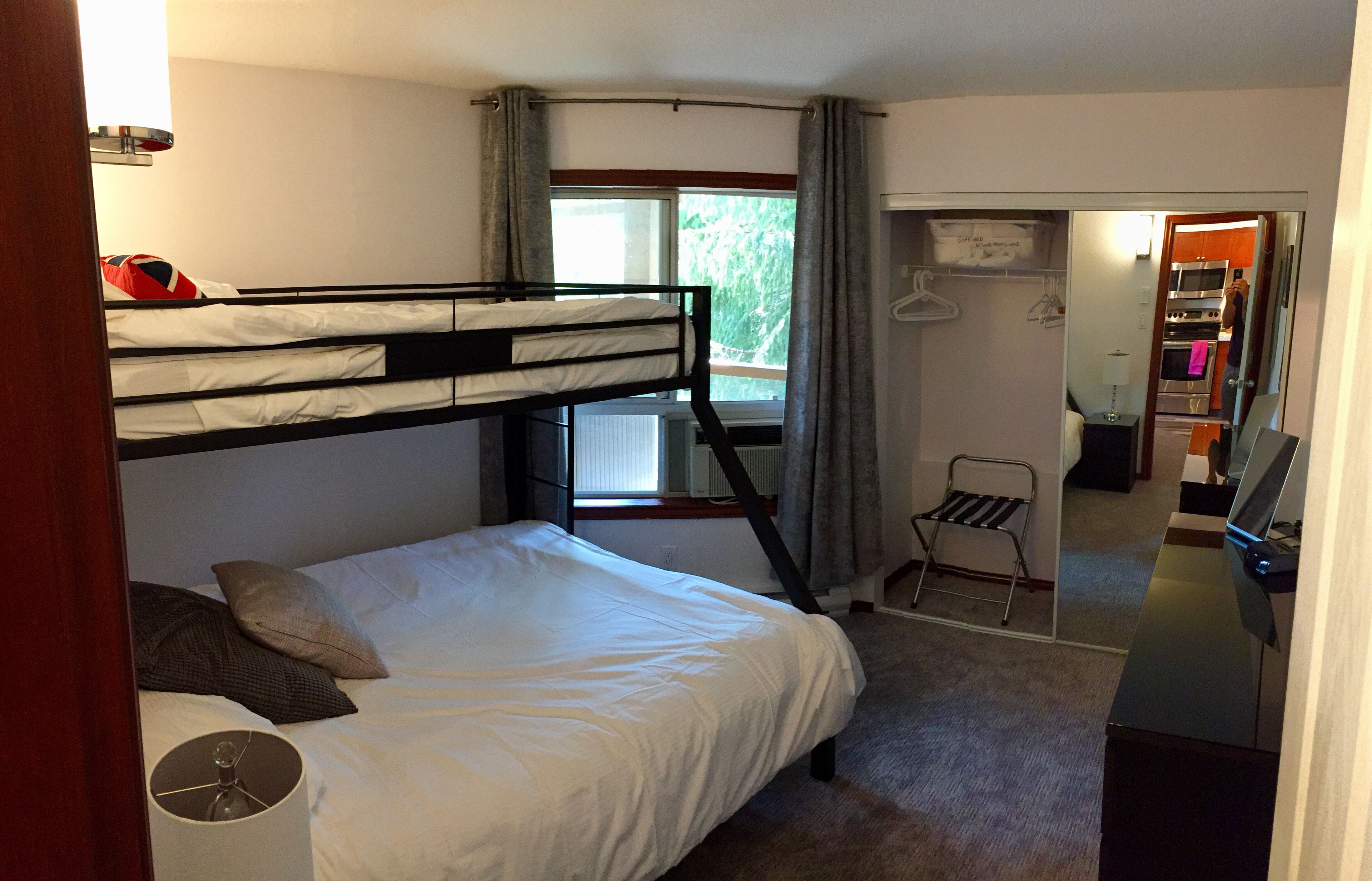 Une chambre avec un lit superposé, un bureau, une chaise et une petite kitchenette.