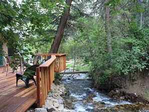 A wooden deck with a wooden bridge over a stream, surrounded by trees.